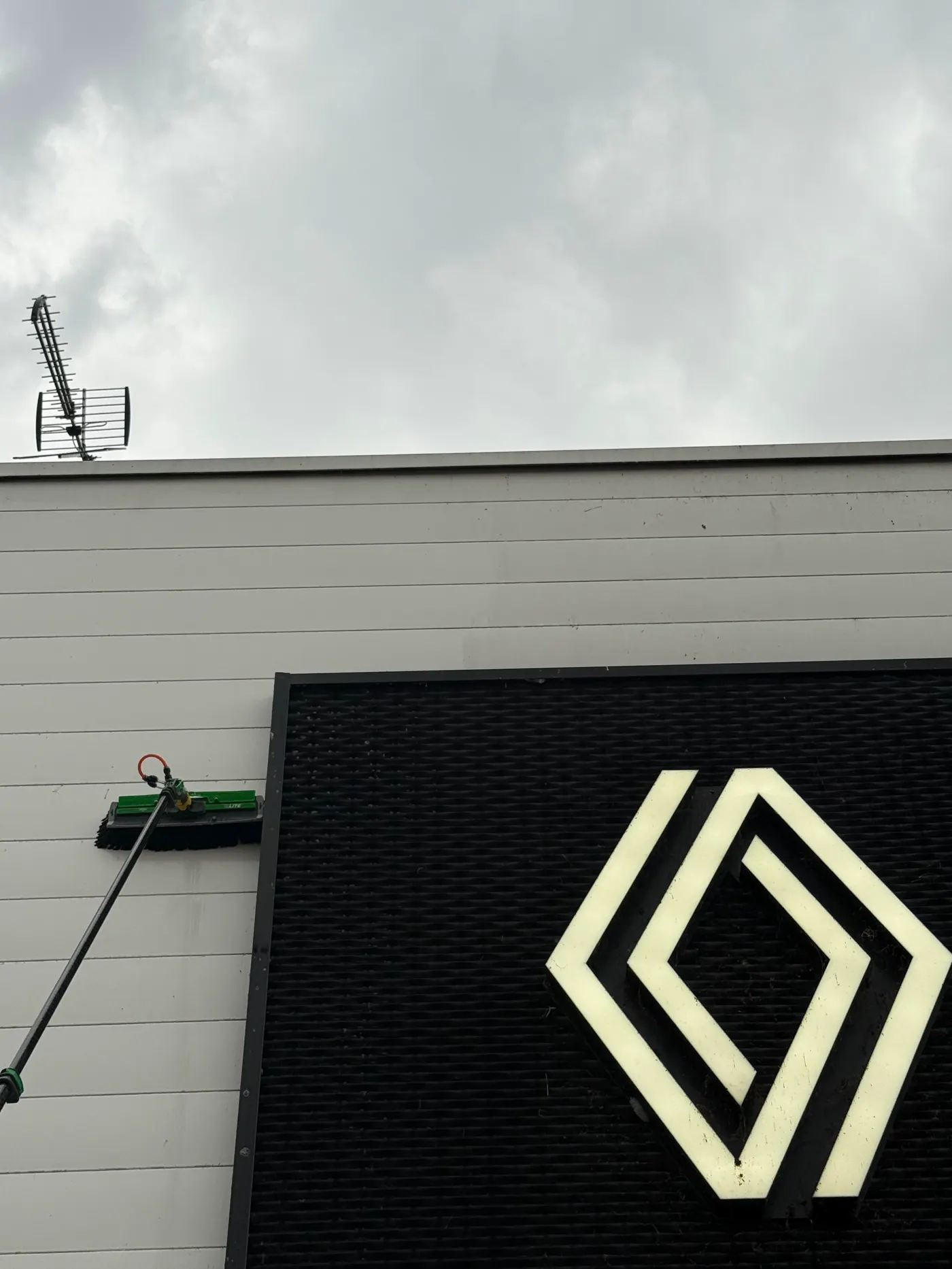 Nettoyage d’une enseigne lumineuse au matériel télescopique, depuis le sol.